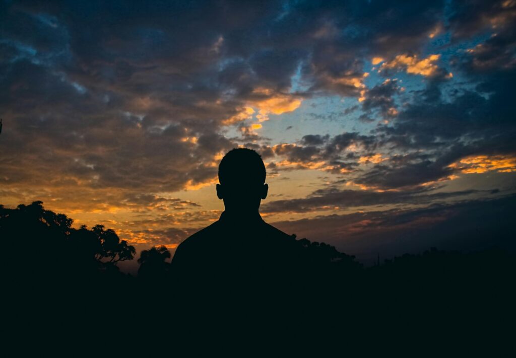 Silhouette of a man against a colorful sunset sky with clouds. Perfect for serene, introspective themes.